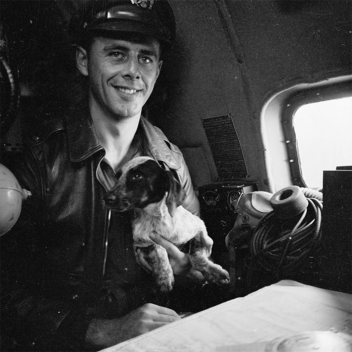 Lieutenant Paul Seramur of Milwaukee, Wisconsin, at the navigator table in a Consolidated B-24 Liberator warplane during the Alexishafen strike. He is holding his pup, Cobber. Alexishafen was a Japanese occupied airbase located on the northeast coast of New Guinea (present day Papua New Guinea), near Madang
